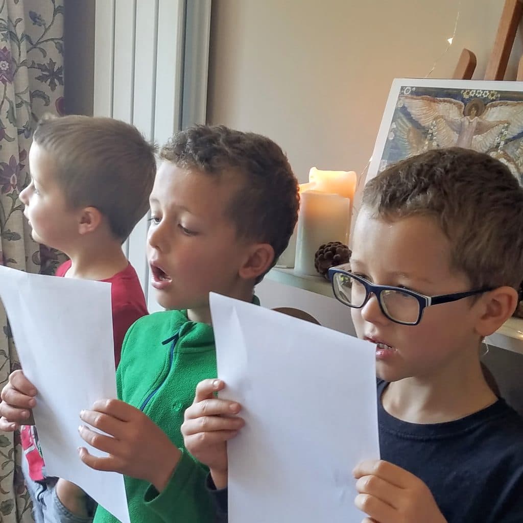 three boys holding music and singing with christmas decorations in background