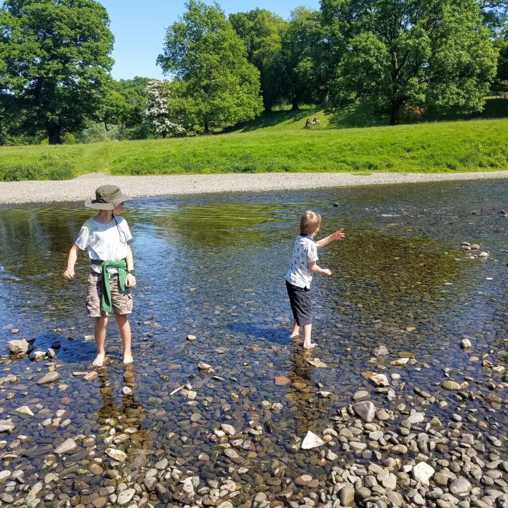 Two boys playing in a river outside - enjoying Charlotte Mason homeschooling to the max.